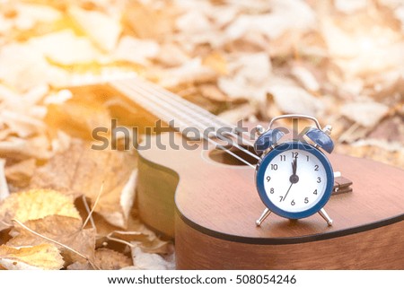 Retro Alarm on Ukulele Guitar on Autumn Leaves Background. Time for Music Concept. Copy space.