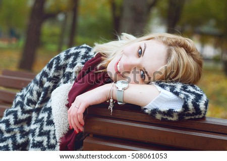 Cute smiling blond woman in black and white knitted warm cardigan relaxing  in autumn park