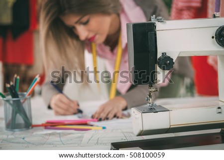 Young woman, fashion designer drawing sketch for new model. Selective focus. Focus on foreground, on a sewing machine.