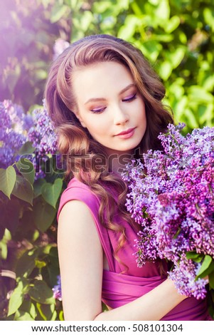 Young beautiful girl posing near lilac bushes in blossom