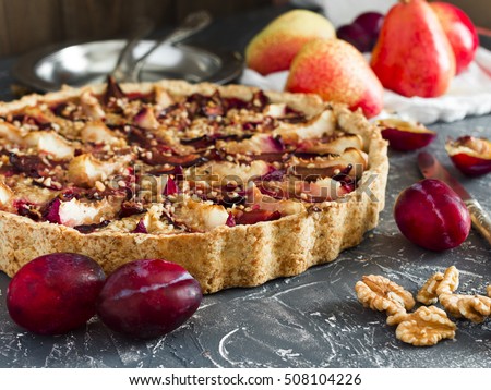 sweet shortbread tart with plums and pears on grey desk with fruits and nuts around Royalty-Free Stock Photo #508104226