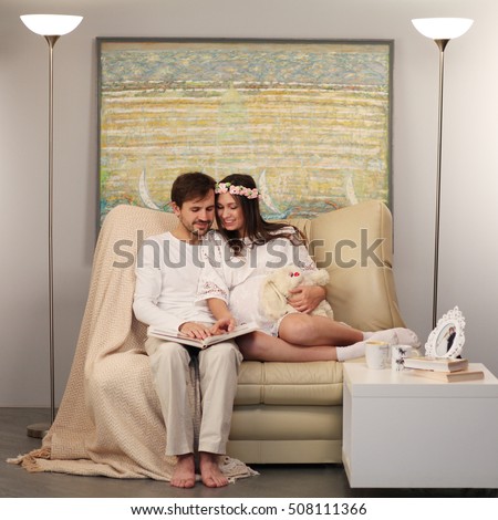 Happy pregnant couple embracing in the background of the paintings in the style of avant-garde.