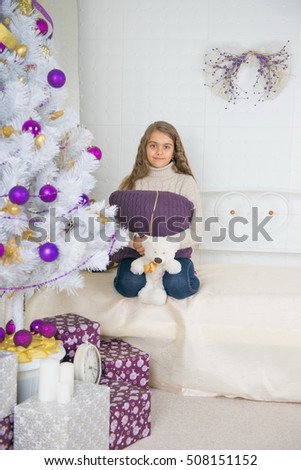 Girl sits on a couch near the Christmas tree. New Year. Waiting for a miracle. Merry Christmas. Home comfort. Girl teenager with long hair sitting on the sofa waiting for Christmas