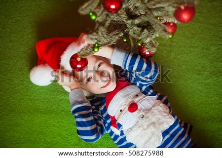 Happy little boy is lies near fir-tree. New Year's holidays.  in a striped T-shirt with Santa Claus