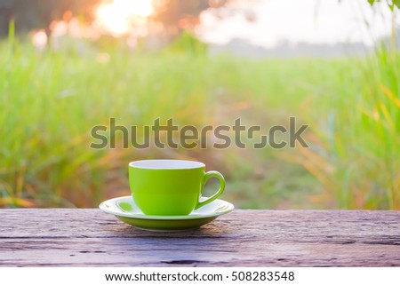 a selective focus picture of a cup of coffee on wooden table in green rice field