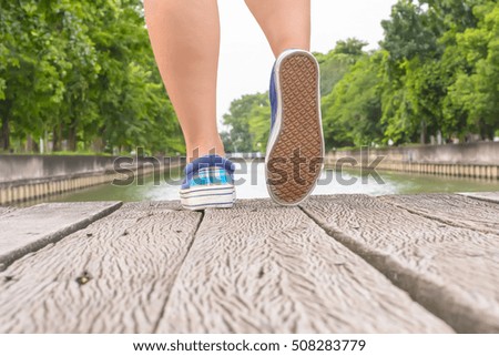 Girl wearing canvas sneakers standing on the wooden bridge.