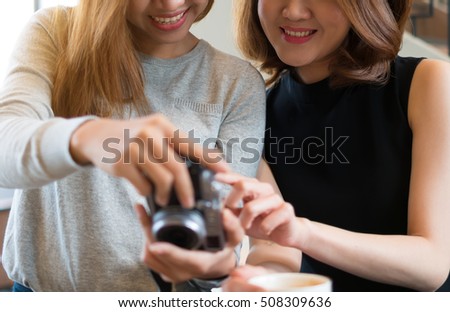 Happy charming women are checking and looking at their picture on the camera LCD display screen with a big smile after shooting in the coffee shop cafe. Feeling funny and happiness.