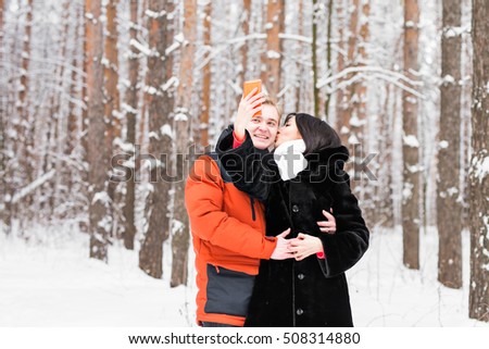 Happy couple in winter taking pictures of themselves with smartphone