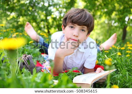 preteen boy reading book in the blossoming spring meadow with dandelions close up portrait