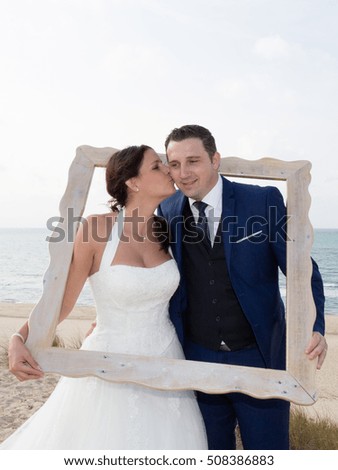 Kissing wedding couple looking through a picture frame