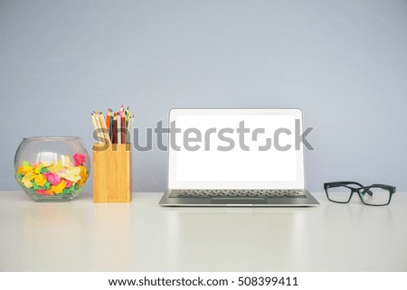 Close up of office desktop with blank white laptop, spectacles, colorful pencils in wooden box and decorative glass bowl. Mock up