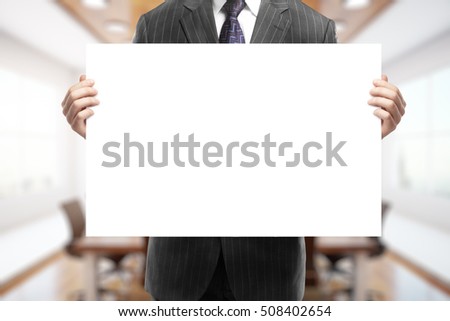 Businessman holding blank poster on blurry conference room background. Mock up