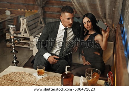 Beautiful elegant young couple relaxing in a bar and smokes a hookah. Are photographed themselves on the phone