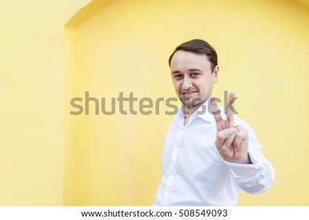 man in the white shirt on a yellow background shows the sign of victory