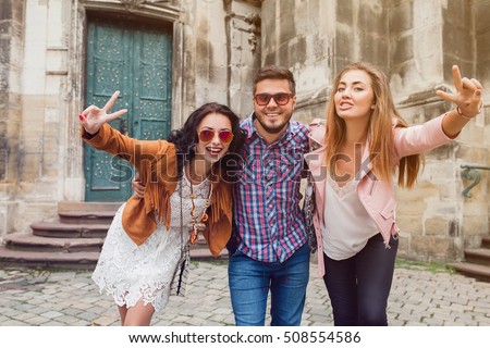 young hipster company of friends traveling, vintage style, europe vacation, sunglasses, old city center, happy positive mood, smiling, embracing, waving hands, looking forward, showing peace sign