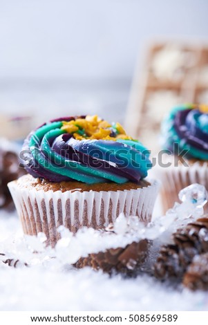 Winter cupcakes with gradient cream and golden stars on a snow with presents, cone and snowflakes on a background. Close view. Vertical shot.