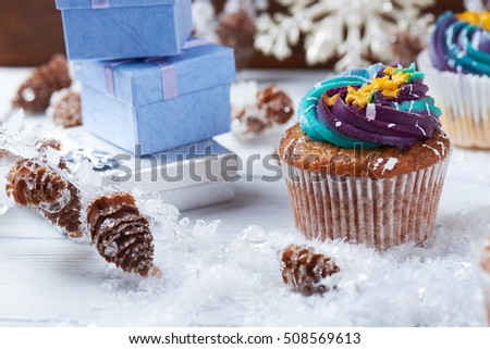 Winter cupcakes with gradient cream and golden stars on a snow with presents, cone and snowflakes on a background. Close view.