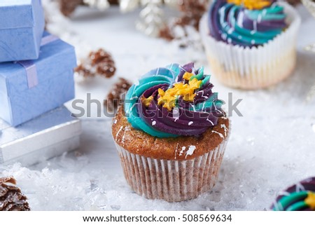 Winter cupcakes with gradient cream and golden stars on a snow with presents, cone and snowflakes on a background. Close view.