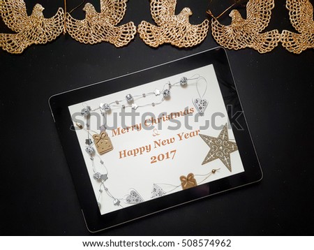Christmas background with gold toy birds decorations and tinsel on black background with tablet and Merry Christmas and Happy New Year, top view and flat lay