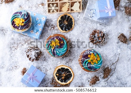 Winter cupcakes with gradient cream and golden stars on a snow with presents, wooden toys, cone and snowflakes on a background. Winter mood. Top view