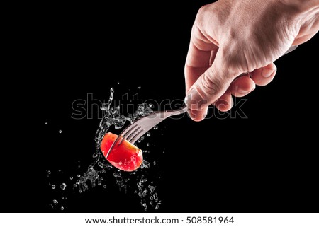 fork with embedded tomato on a black background splashing water