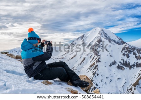 Man in ski suit taking photos of mountain landscape with smartphone.