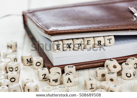 Word EXPERT written on a wooden block in a book. On old wooden table.