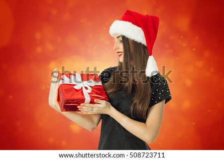 beauty woman in santa hat smiling with red gift in hands on red background