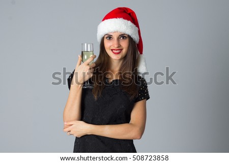 young girl with glass of champagne in santa hat in studio on grey background