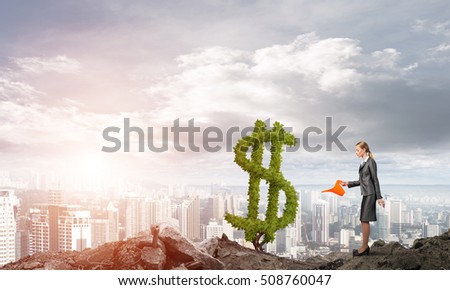 Young attractive businesswoman watering plant in ground with can against the backdrop of the city
