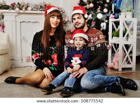 mother, father and little boy with red Christmas hat on the background of the Christmas tree