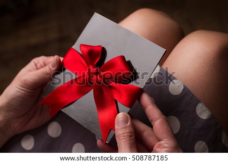 Close up of the hands of a woman with polka dress holding a black card with red ribbon above knees Royalty-Free Stock Photo #508787185