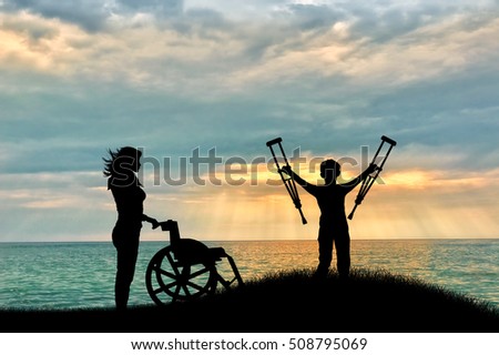 Child disabled with crutches beside wheelchair and nurse on beach on hill. Concept help.