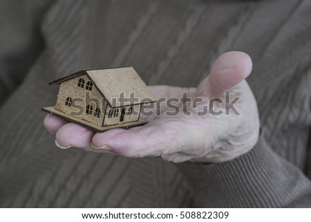 house, closeup wrinkled hand of an old senior woman or man holding a tiny small wooden house on palm. home ownership concept photo with old people in retirement age