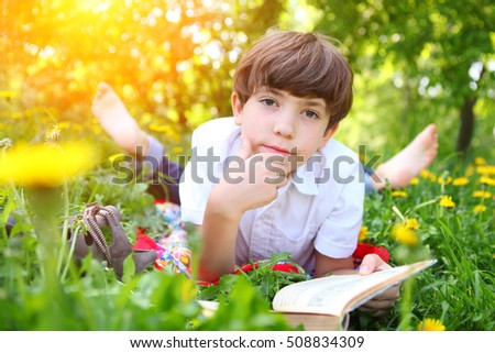 preteen boy reading book in the blossoming spring meadow with dandelions close up portrait