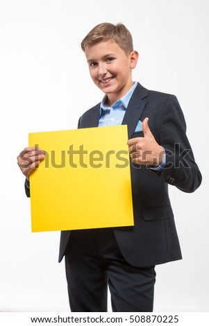 Emotional blond boy in a suit with a yellow sheet of paper for notes on a white background