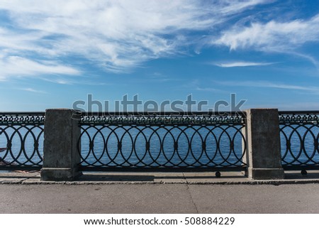 Wrought iron railings with concrete pillars against the blue sky with clouds. Symmetry, background, concept.