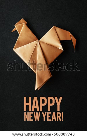 Golden shiny paper folded rooster handmade origami craft on black background. Nice natural holiday greeting card. Happy new year lettering.