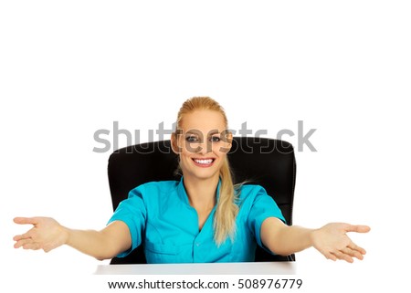 Funny female doctor or nurse sitting behind the desk with open arms
