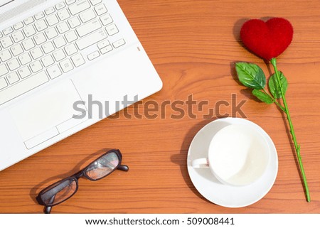 Artificial red heart flower, glasses, laptop and coffee cup on wooden floor