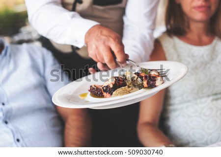 Waiter serving a plate of Greek Grilled octopus to a men guest in a restaurant.
