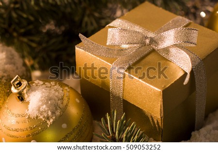 Christmas and New Year`s festive concept. Gold gift box with silver bow, toy balls, fir cones and tree branches covered with snow. Greeting card Background with holiday tinsel.