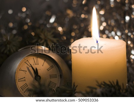 Christmas and New Year`s clock showing five to midnight. Festive evening candle. Christmas tree fir branches covered with snow. Concept for congratulations and party with copyspace for text or logo.
