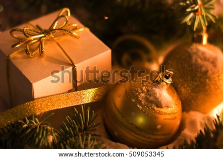 Christmas and New Year`s concept. White gift box with gold bow, toy balls, fir cones and tree branches covered with snow. Greeting card Background with holiday tinsel.
