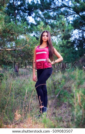 Young beautiful brunette model posing in the sports image of the park against the backdrop of trees on the portrait photo shoot