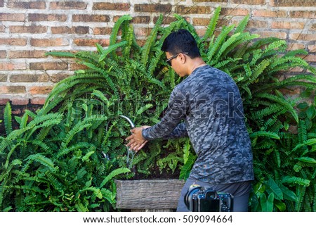 Photographer man washing his hands at wooden sink ornamented with fern next to old brick wall.