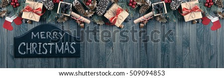 Christmas background with signboard and inscription, spruce, gift box, Santa Claus boots, mitten and scroll in vintage style on wooden shabby boards with place for text.  