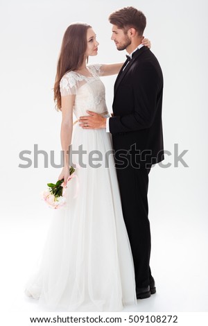 Full-length portrait of pretty newlyweds with bouquet. isolated white background