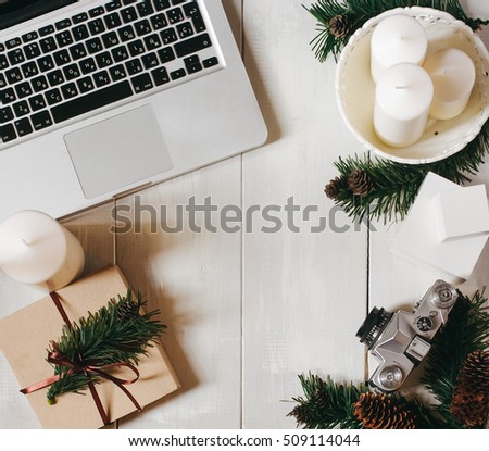 workspace in christmas style with laptop, white candles, decorative gifts and spruce branches and cones on white wooden background. Freelance and work on holidays concept. Top view, Flat lay