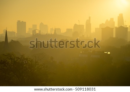 Golden sunrise skyline of London, England featuring modern skyscrapers peeking up above misty parkland trees